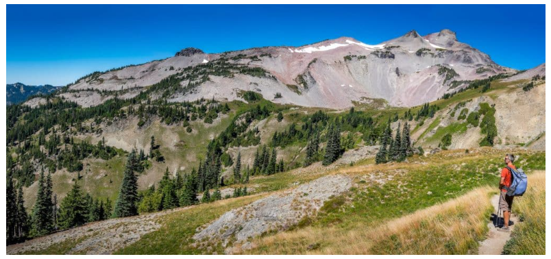 Clint hiking along a mountain ridge trail with a backpack, gazing at the peaks